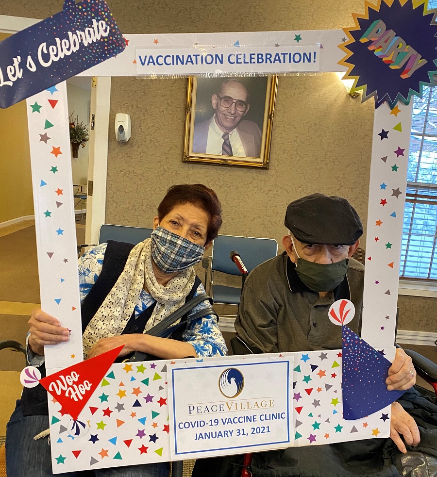 Two seniors in masks holding vaccine celebration sign